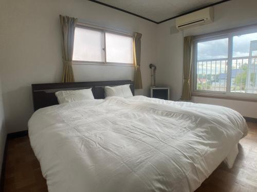 1 cama blanca grande en un dormitorio con 2 ventanas en 落ち着きのある安らぎ空間／新千歳空港から30分の一棟貸し民家, en Chitose