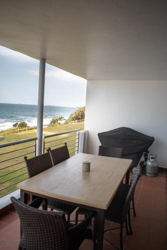 a wooden table and chairs on a balcony with the ocean at Palm Cove - 16 Chakas Cove, Literally on the Beach in Ballito