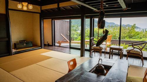 a living room with a table and chairs and windows at 森の入り江の離れ宿 無雙庵枇杷 in Toi