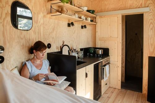a woman sitting in a kitchen reading a book at L'Atelier Tiny House Provence in Châteaurenard