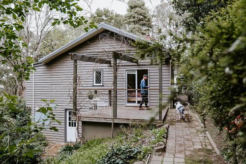 a man standing on the porch of a house with a dog at Romantic Getaway - 2 luxe outdoor baths in Mount Macedon