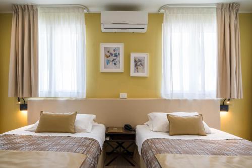 two beds in a room with yellow walls and windows at Hotel Rivage Taormina in Taormina