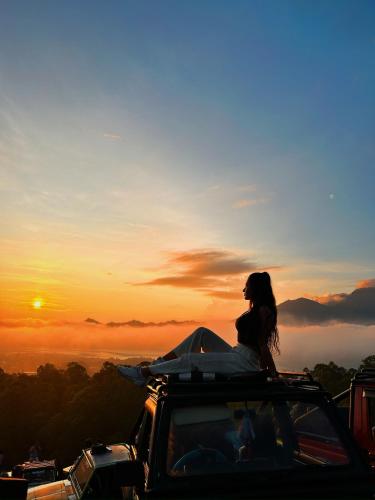 a woman sitting on the roof of a car watching the sunset at Batur Volcano Guesthouse in Kintamani
