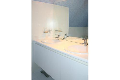 uma casa de banho branca com 2 lavatórios e um espelho em Albatros D2 em De Haan