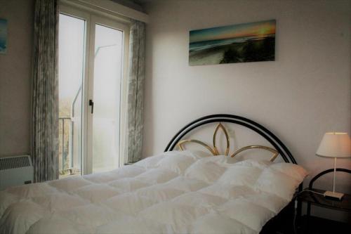 1 cama blanca en un dormitorio con ventana en Golf & Strand C2, en De Haan