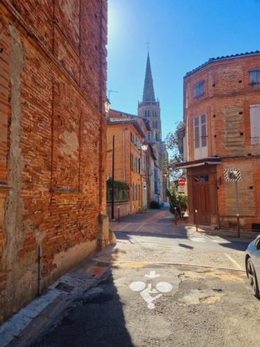 an alley with a brick building and a church at chambres d'hotes Le 1891 in Montech