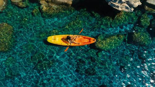 a yellow surfboard in the water next to some rocks at Alexandros Palace in Ouranoupoli