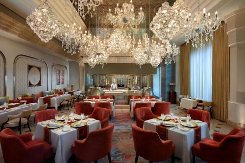 a restaurant with white tables and red chairs and chandeliers at The Leela Gandhinagar in Gandhinagar