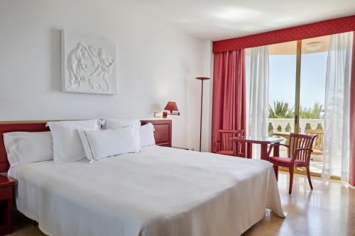 a bedroom with a white bed and a table and chairs at Hotel Cleopatra Palace in Playa de las Americas