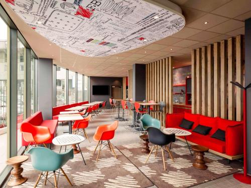 a waiting room with red chairs and tables and tablesktop at ibis Lyon Carre De Soie in Vaulx-en-Velin