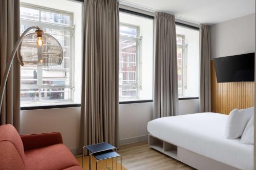 a hotel room with a bed and a chair and windows at Motto By Hilton Rotterdam Blaak in Rotterdam