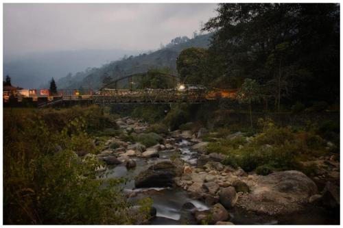 een trein over een brug over een rivier met rotsen bij Jharna Natural Homestay Mirik in Mirik