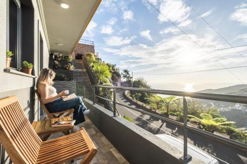 a woman sitting on a balcony looking out at the ocean at Il Tramonto by Homie in Ribeira Brava