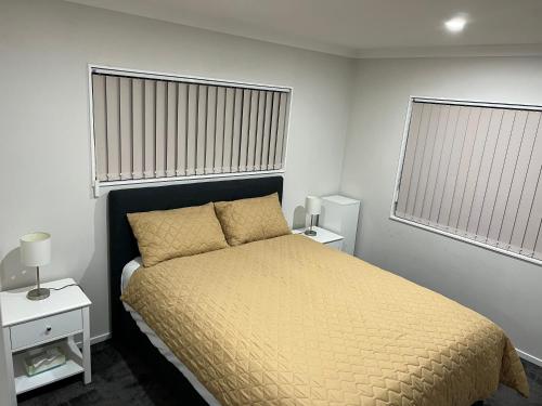 a bedroom with a bed with a yellow bedspread and two windows at Private resident in Auckland