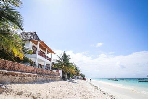 a beach with a building and palm trees and the ocean at Babu Villas in Jambiani