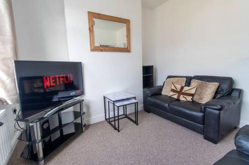 a living room with a black leather couch and a television at Station 14 - Vacation Home in Gelligaer