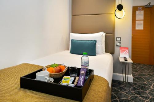 a hotel room with a tray of food on a bed at Queens Park Premier London Hyde Park in London