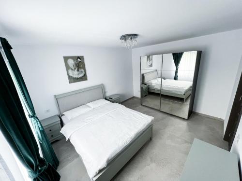 a white bedroom with a bed and a mirror at Casa Maya in Curtea de Argeş