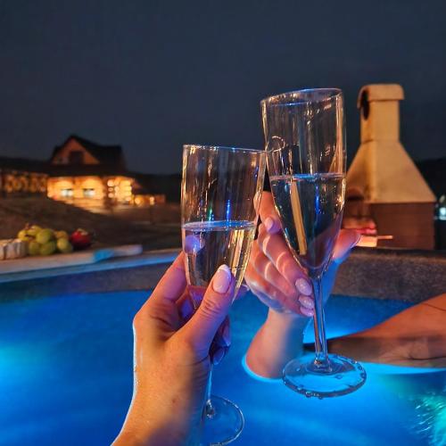 two people holding wine glasses next to a swimming pool at NOVAK CHALET domki z balią Krynica Zdrój in Krynica Zdrój