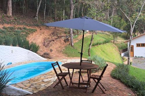 a table and chairs with an umbrella next to a pool at Orobó Kaá - entre a floresta e a vida no campo in Monteiro Lobato