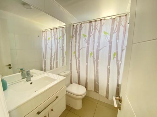 a bathroom with a toilet and a shower curtain with trees at Departamentos en la PLAYA in La Serena