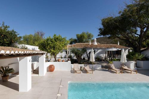 a pool with chairs and umbrellas next to a house at Âmago Guesthouse in Santa Bárbara de Nexe