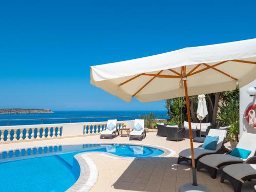 a pool with chairs and an umbrella and the ocean at Villa Palma - Sunset Sea Views with Pool, Jacuzzi, Sauna and Games Room in Mellieħa