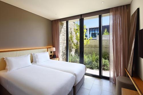 two beds in a hotel room with a large window at Minthis Resort in Paphos City