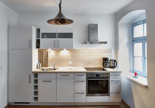 eine Küche mit weißen Schränken, einer Spüle und einer Leuchte in der Unterkunft Ferienwohnung Priessnitz in Dresden