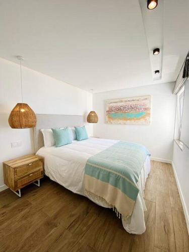 a white bedroom with a bed and a night stand at Front Sea Apartment Quarteira in Quarteira