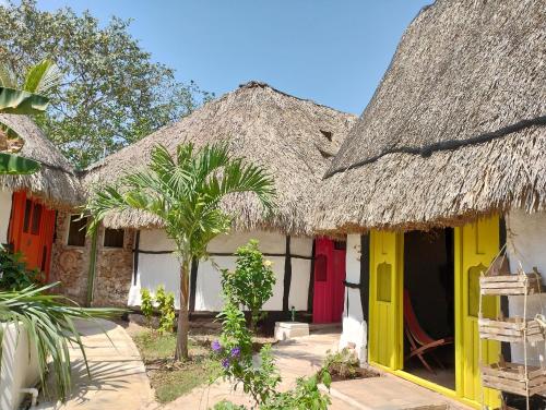 a couple of houses with thatched roofs and a palm tree at Hotel y Museo Aldea Maya Toktli Orígenes - Casa Maya Melipona - Alberca, Wifi Starlink, Tour Museo in Izamal