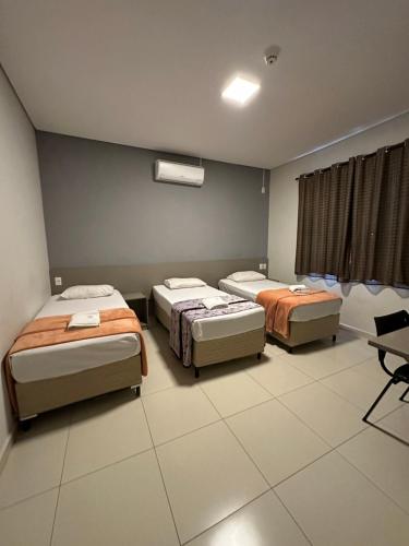 a room with three beds and a desk and a window at Shafira Hotel in Limeira