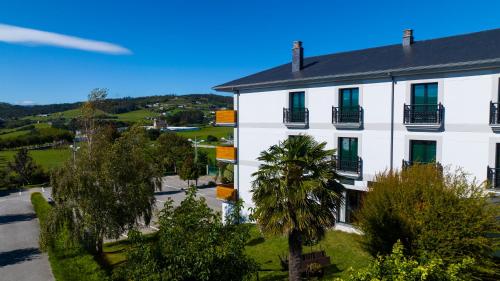 a white building with green shuttered windows and trees at Hotel O Cabazo in Ribadeo