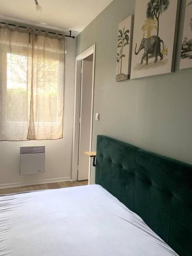 a bedroom with a bed with a green headboard and a window at L'oasis aux portes de Toulouse in Muret