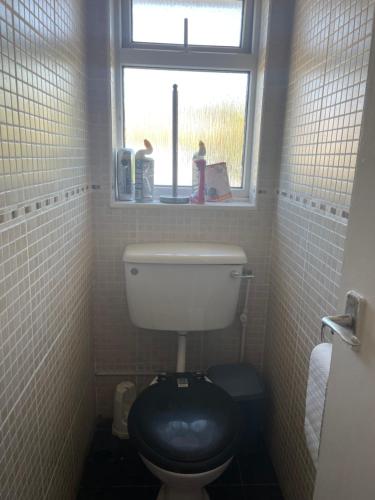 a bathroom with a toilet with a black seat and a window at Cozy Home in Twickenham