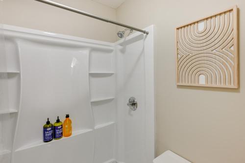 a white bathroom with a shower with bottles on a shelf at Stunning Franklin Cabin with Deck and Mountain Views in Franklin