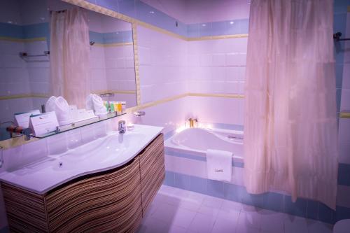 ein Badezimmer mit einer Badewanne, einem Waschbecken und einem Spiegel in der Unterkunft Elite Seef Residence And Hotel in Manama