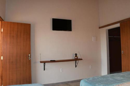 a bedroom with a tv and a shelf on the wall at Chalés Aconchego in Pirenópolis