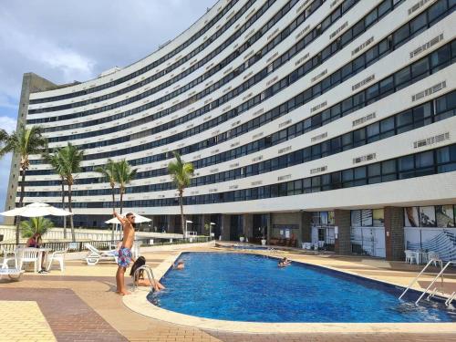 a man standing next to a swimming pool in front of a building at @ondinaapartreservas Pé na Areia 441 in Salvador