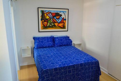 a bedroom with a blue bed with a painting on the wall at Apto frente mar 2 suítes in Rio de Janeiro