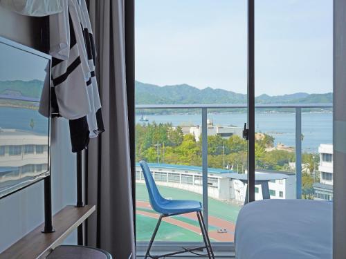a room with a blue chair and a view of a tennis court at SETOUCHI KEIRIN HOTEL 10 by Onko Chishin in Tamano
