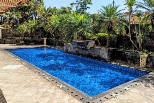 a large blue swimming pool in a yard with palm trees at Cottonwood Japandi Apartment at Majesty 1222 in Bandung