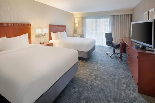 a hotel room with two beds and a flat screen tv at Courtyard Detroit Southfield in Southfield