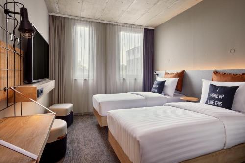 a hotel room with two beds and a television at Moxy Karlsruhe in Karlsruhe