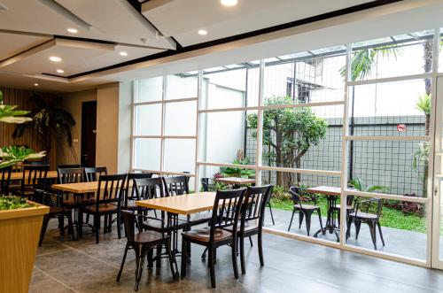 un restaurante con mesas, sillas y ventanas grandes en Arcadia Hotel Manado, en Manado