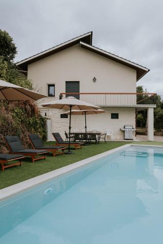 a pool with chairs and umbrellas in front of a house at Casa de Greire in Castelo de Paiva