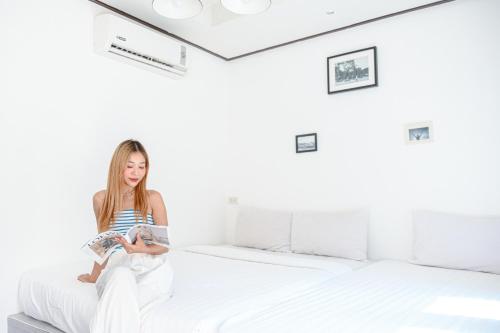 a woman sitting on a bed reading a book at Sidewalk Boutique Hotel in Ko Samed