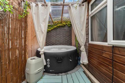 a black bath tub sitting on a deck next to a window at 2BED Garden house w/Hot Tub, Sauna & Cinema room in London