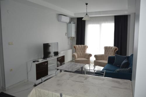 ein Wohnzimmer mit einem TV, einem Sofa und Stühlen in der Unterkunft Hera Rezidans in Kırac
