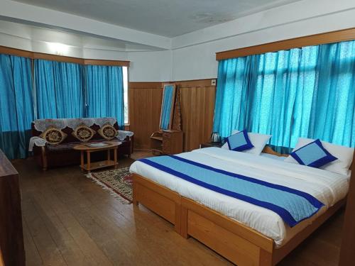 a bedroom with a bed and a couch and blue curtains at Enchanting Tawang in Tawang